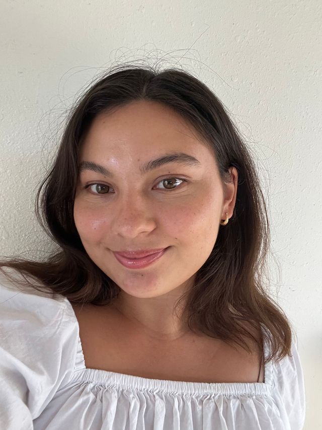 Smiling woman in a white off-shoulder blouse against a plain light background
