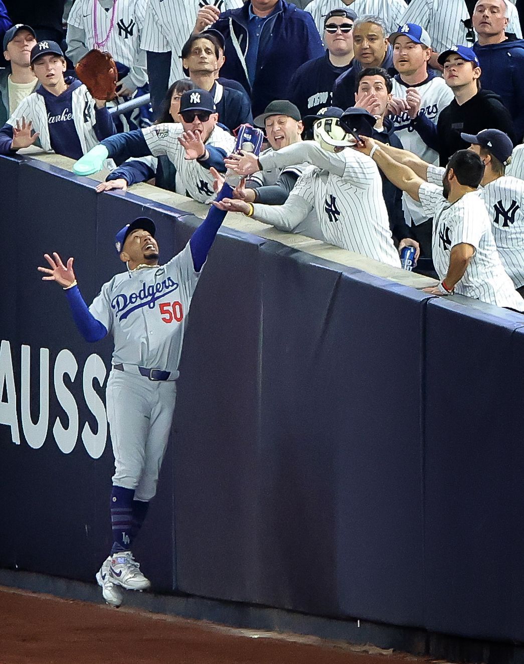 Baseball player jumping to catch a ball near a wall, fans reaching over.