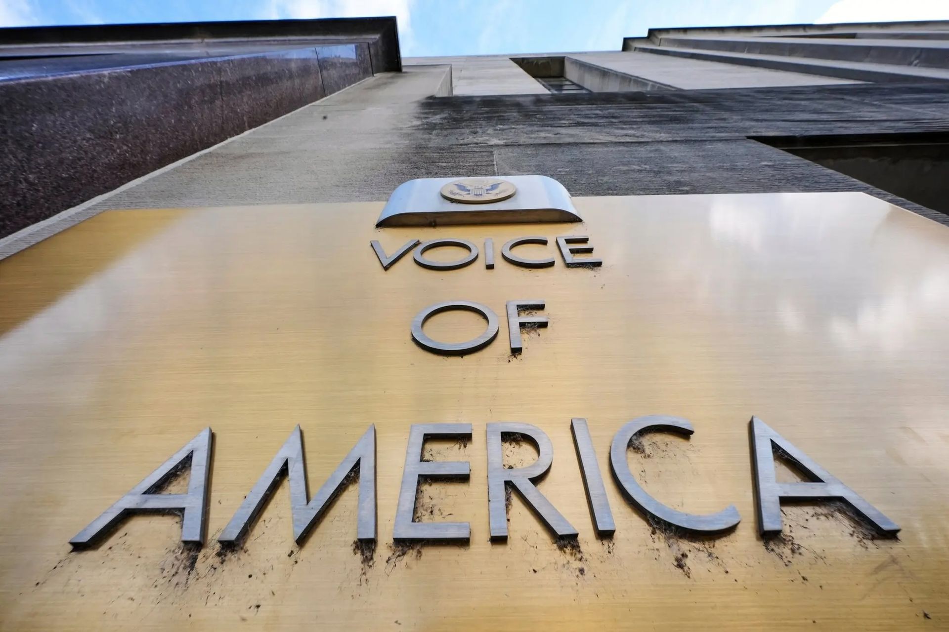 Close-up of the Voice of America sign on a building facade, viewed from below.