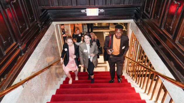 People walking down red-carpeted stairs with wood paneling.