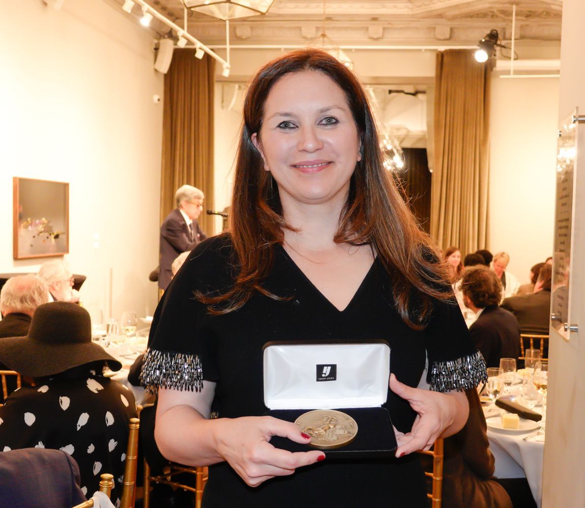 Woman holding a small box with an award at a dinner party, smiling.