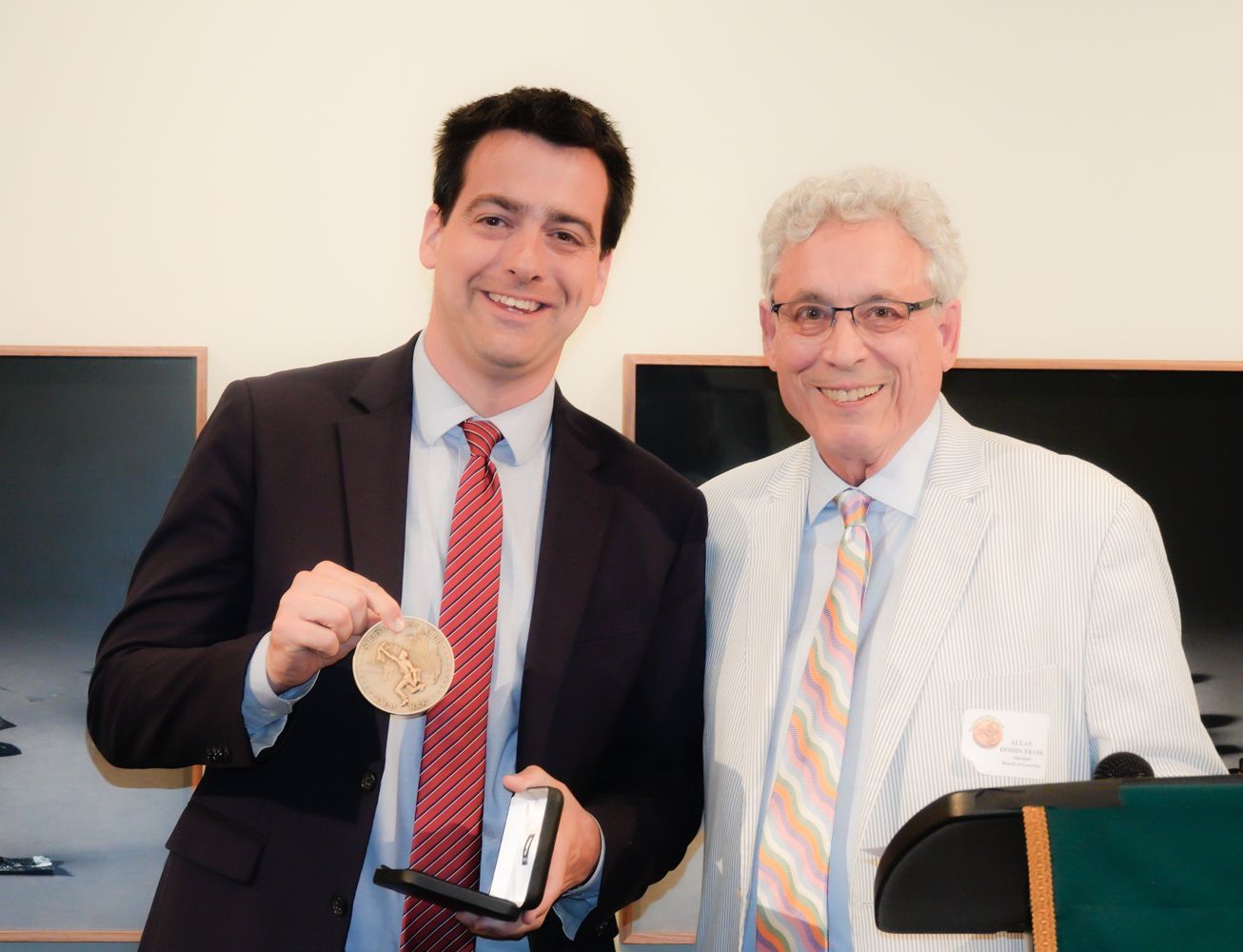Man holding a medal, smiling next to older man in striped jacket.