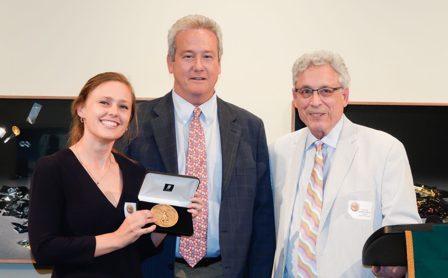 Woman holding medal smiles with two men, interior setting.