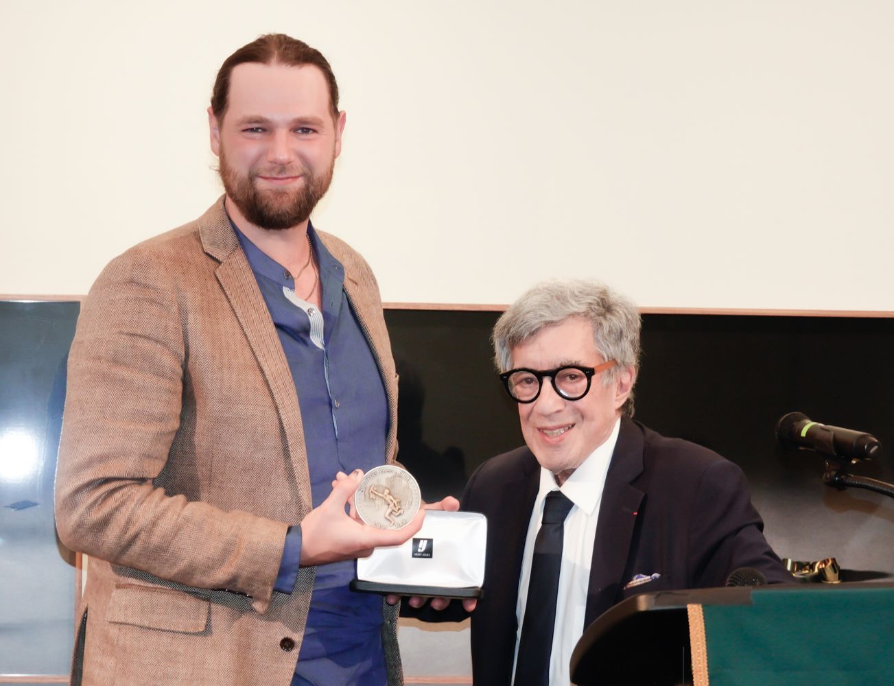 Man in blazer receives award from another at podium.