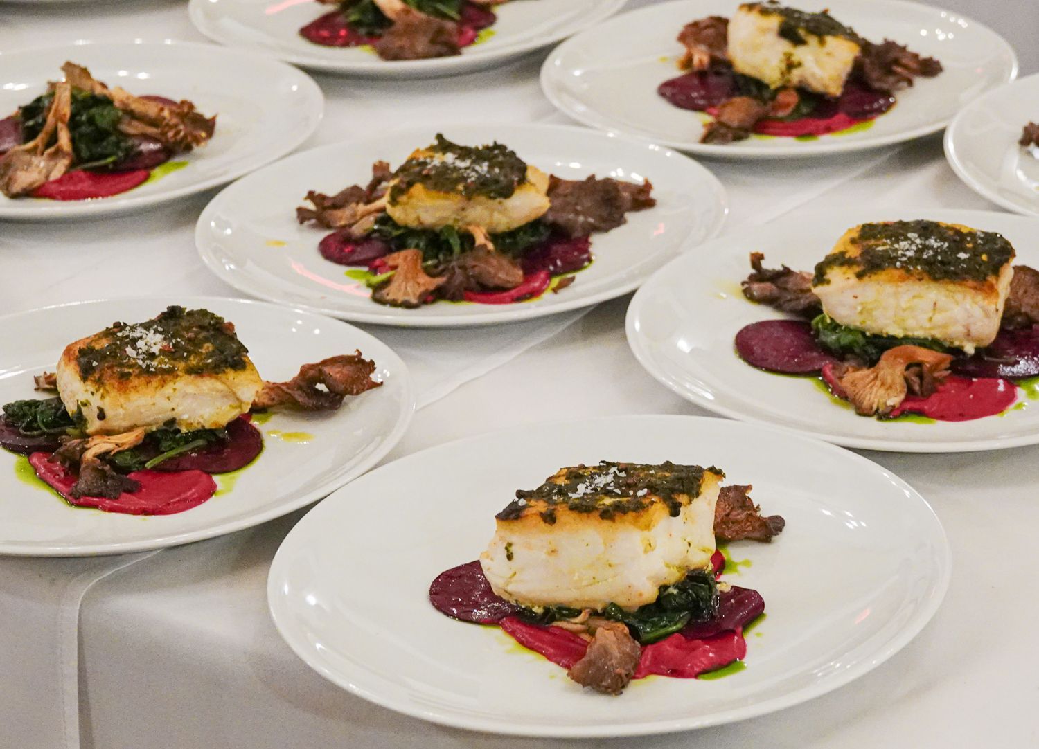 Plated meal: white fish with green herb topping, beet puree, mushrooms, and greens on white plates.