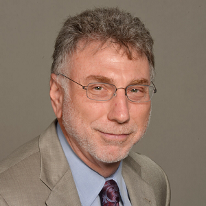Man in suit and glasses smiling; head and shoulders.