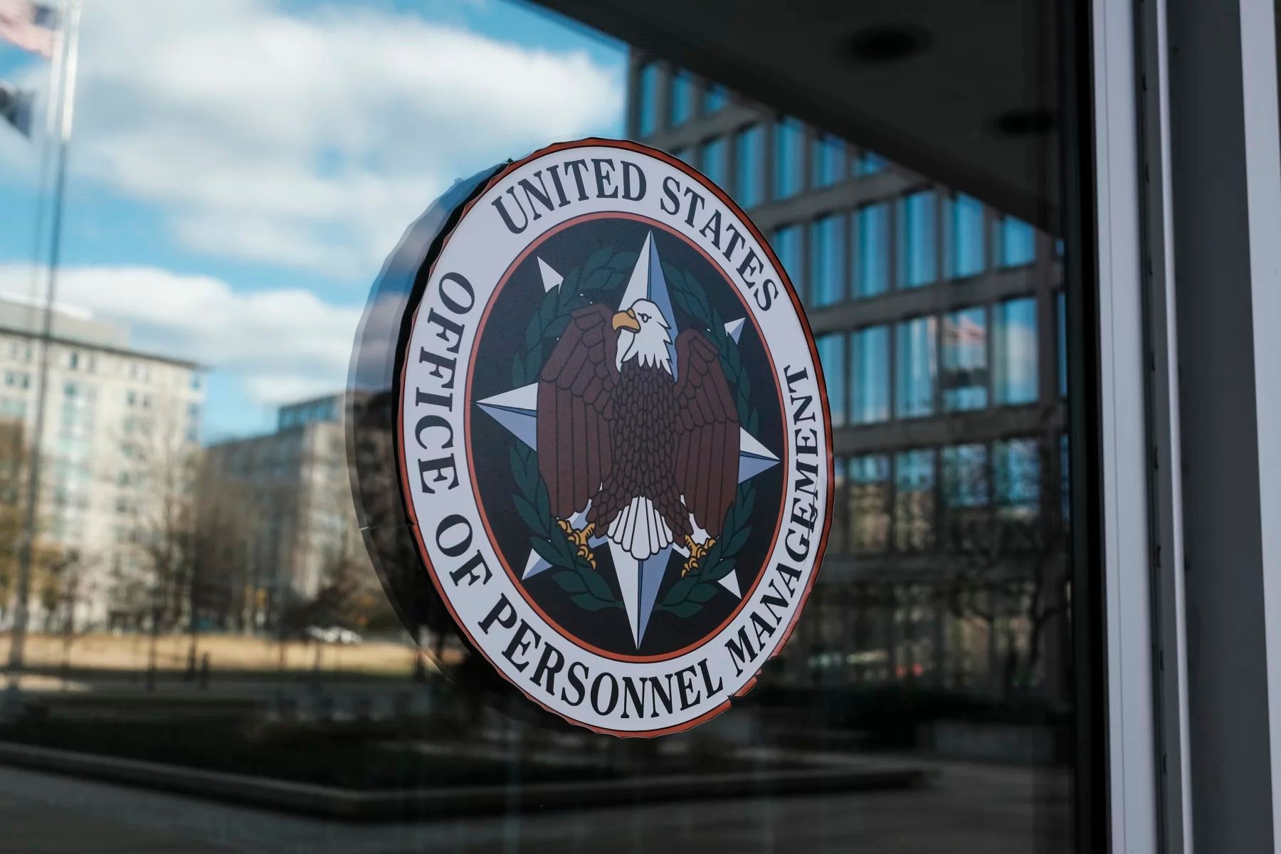 U.S. Office of Personnel Management seal on a glass door, reflecting buildings and sky