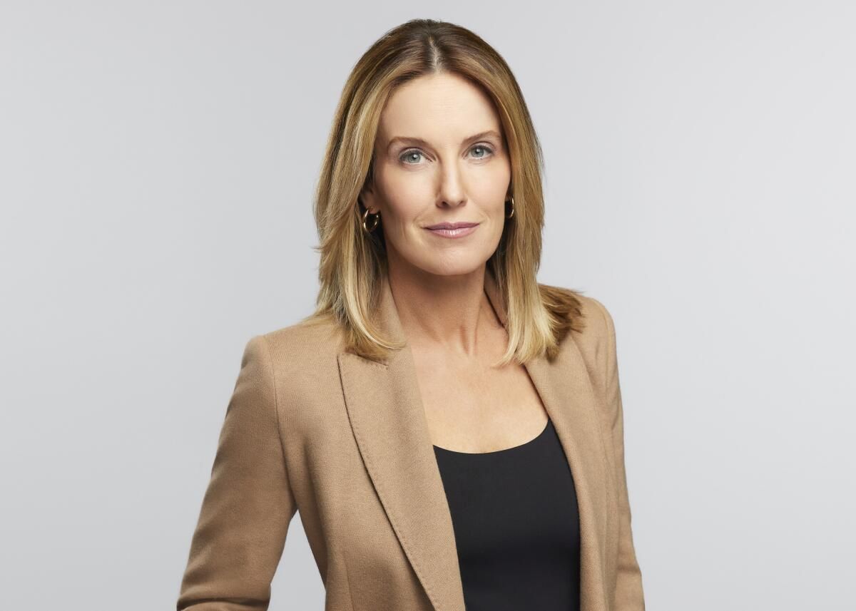 Portrait of a woman in a tan blazer over a black top against a light gray background