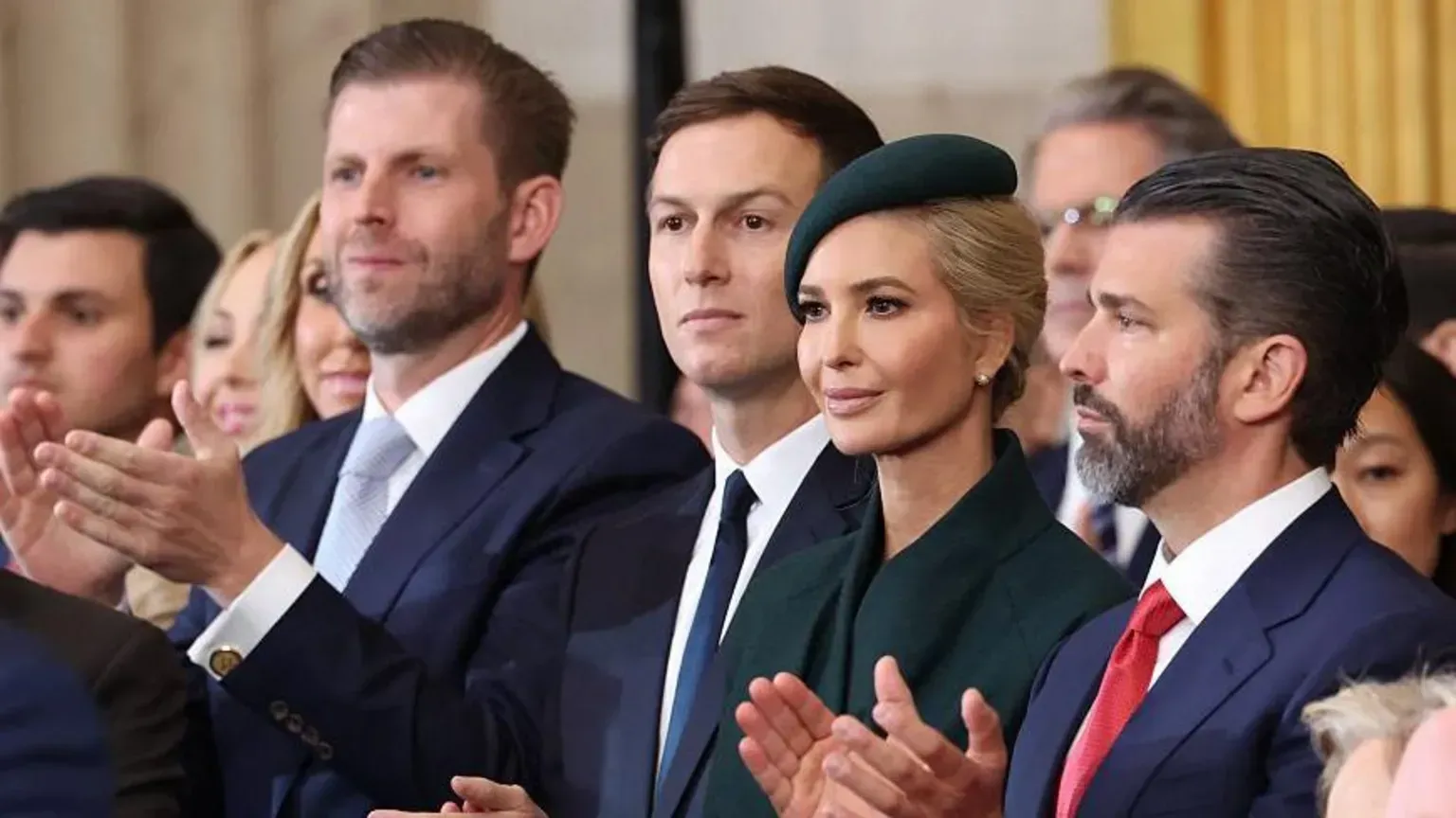 Audience members in formal attire applauding at a public event, seated in a row.
