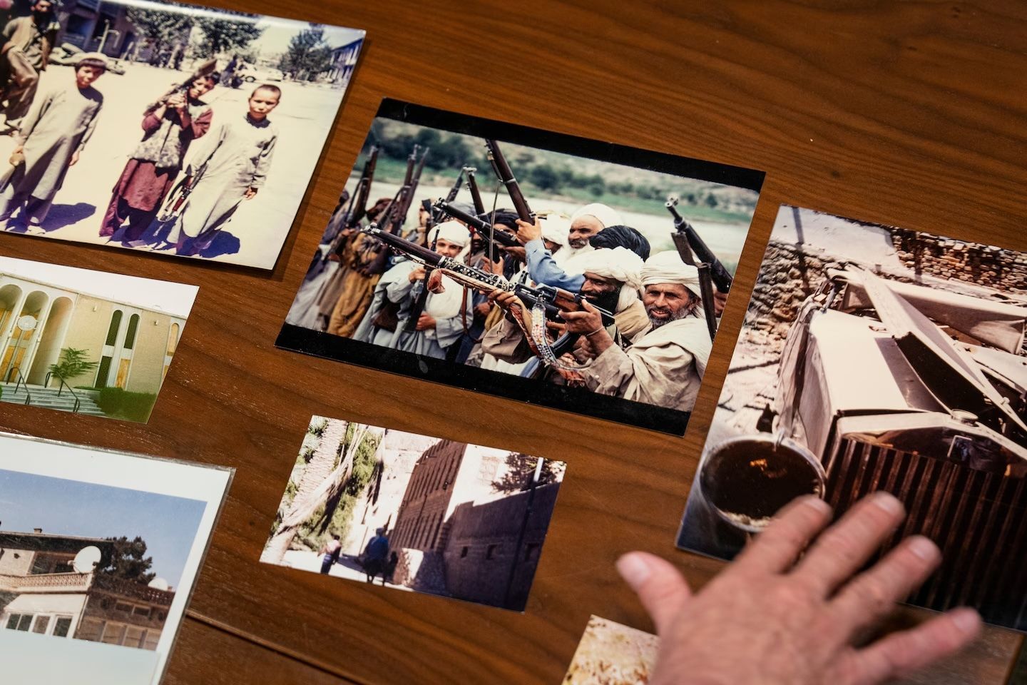 Printed photos spread on a wooden table, with a hand reaching toward a black-and-white photo.