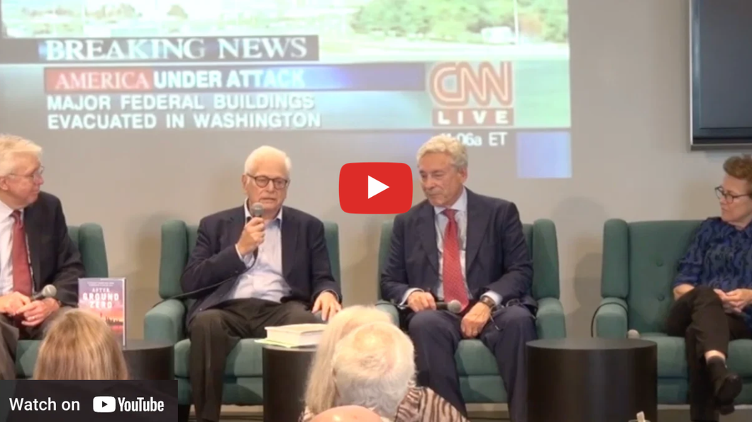 Panel discussion with four men seated on stage, CNN “Breaking News” graphic in background and YouTube play icon overlay
