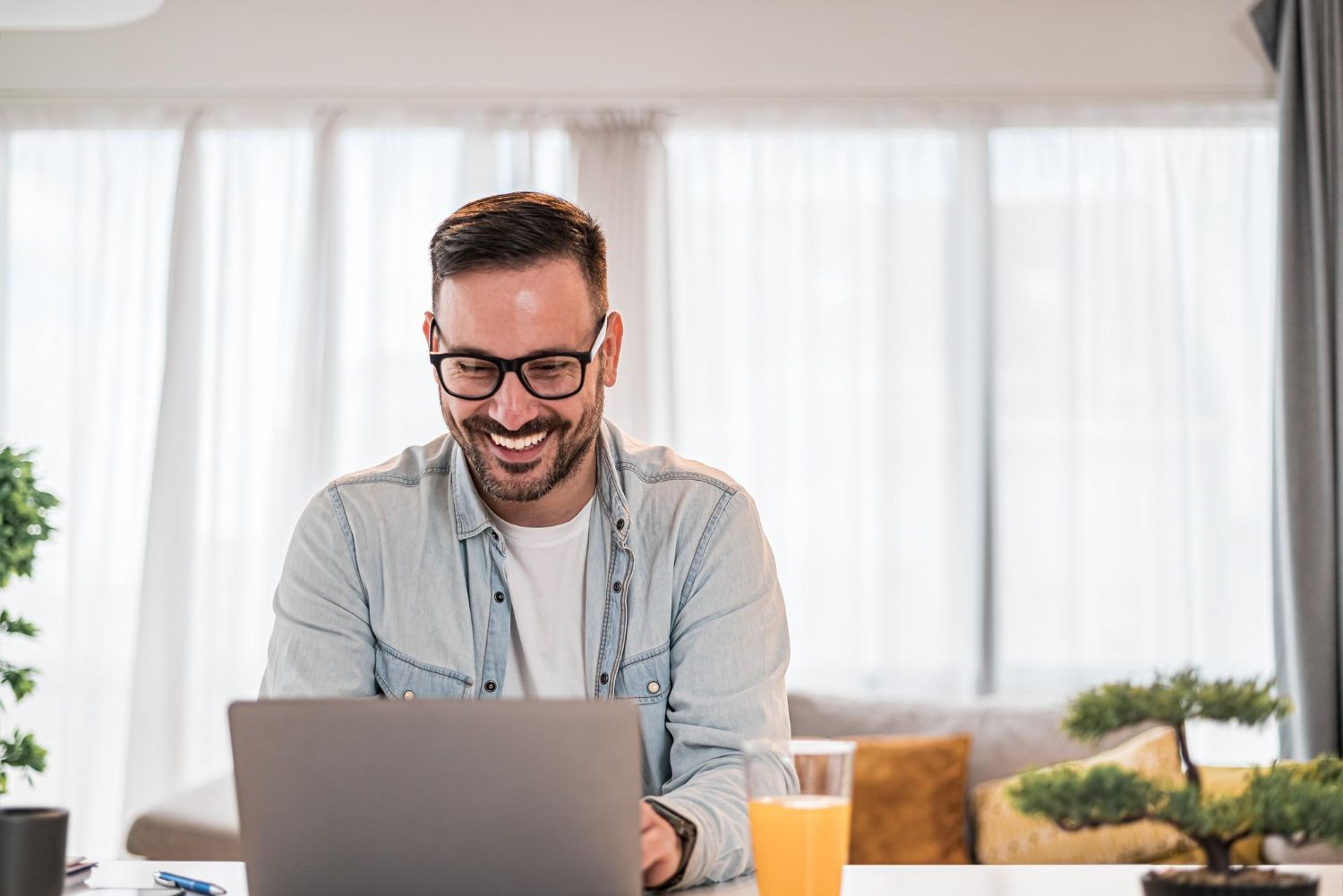 Man smiling while working on a laptop at a bright home desk