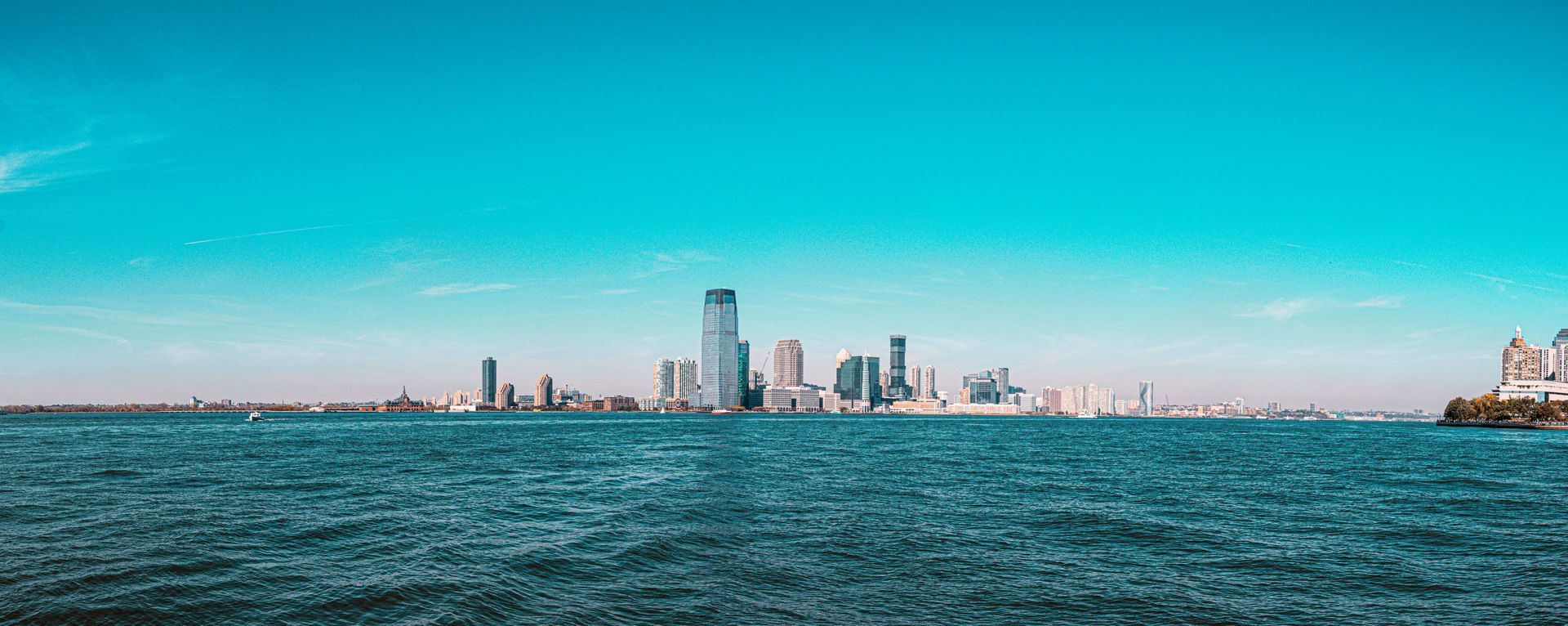 Distant city skyline beyond choppy blue water under a bright turquoise sky