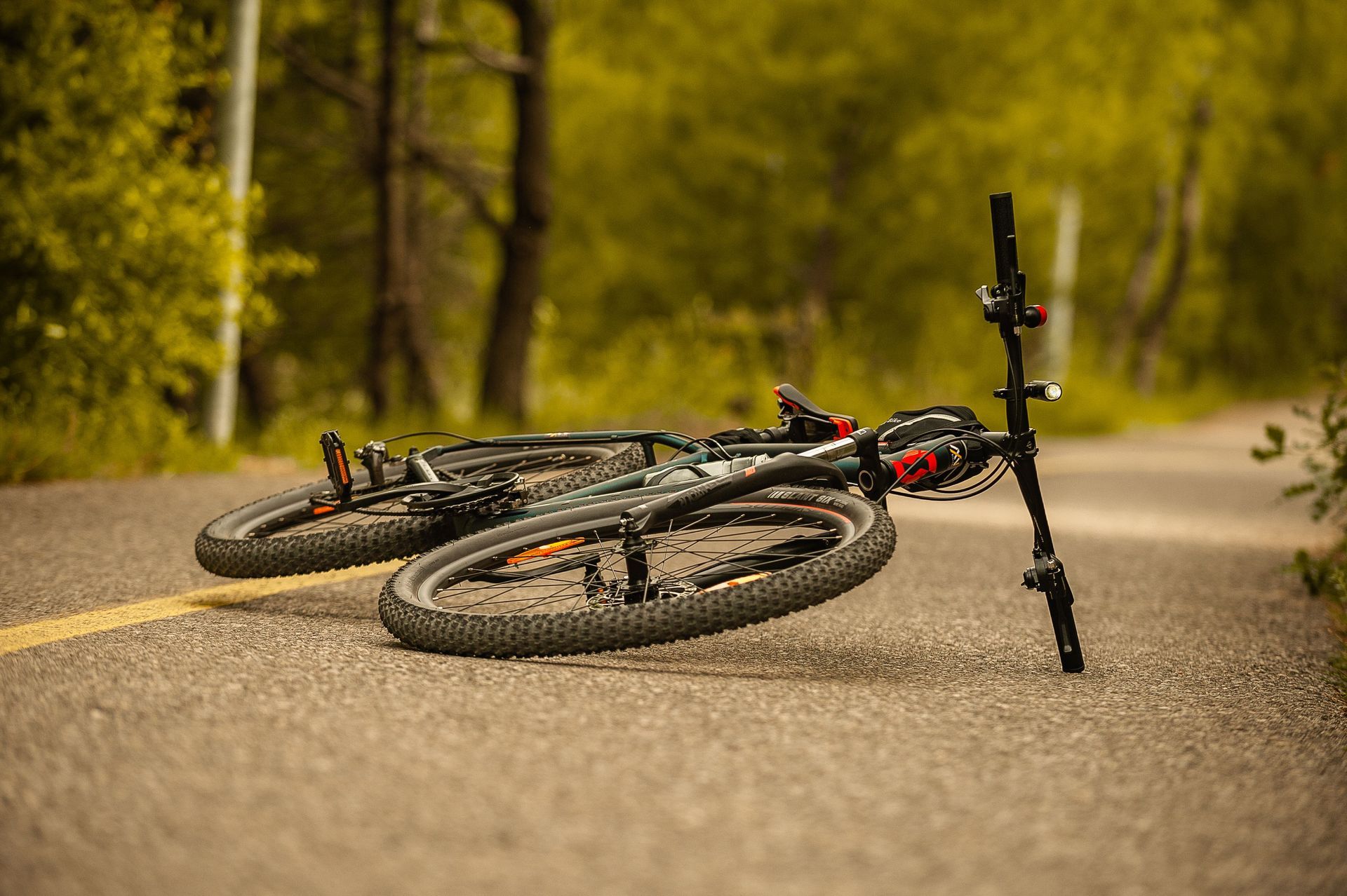 A muddy mountain bike lying on a paved path in a wooded park.