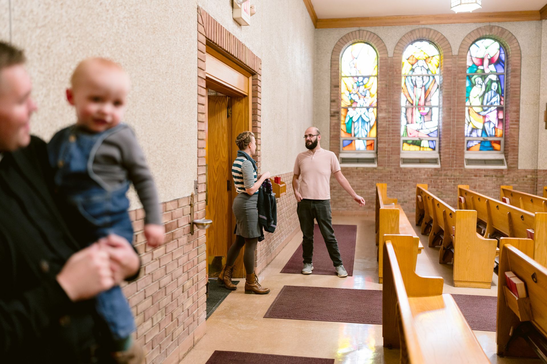 People walking in a church aisle with stained glass windows and wooden pews.