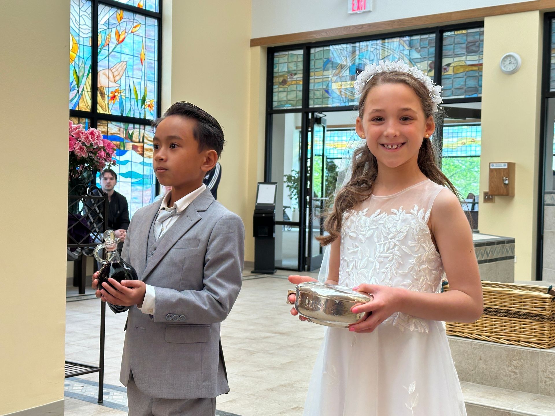 Two children in formal clothes holding rings at a church entrance.