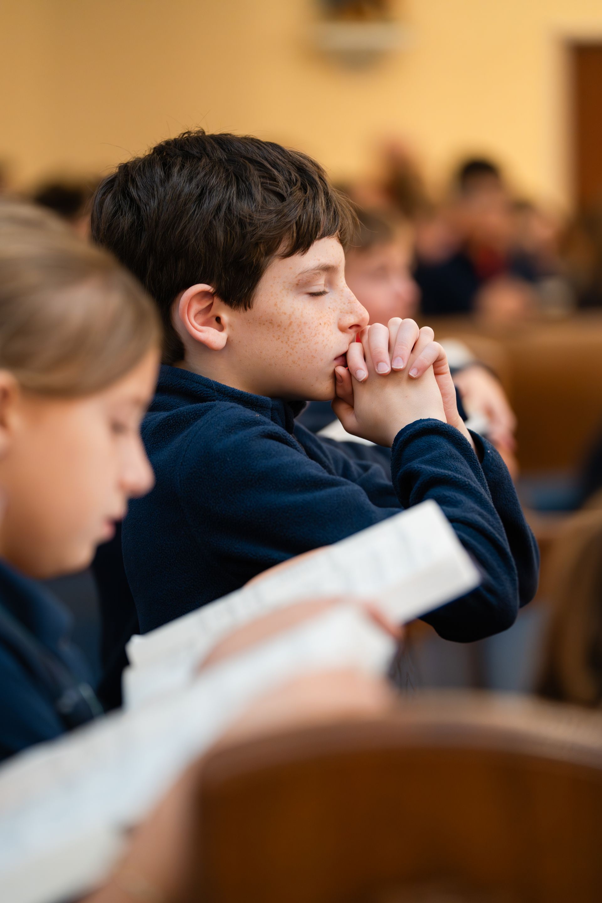 People seated in a church pew, one with hands clasped in prayer and another reading a book.