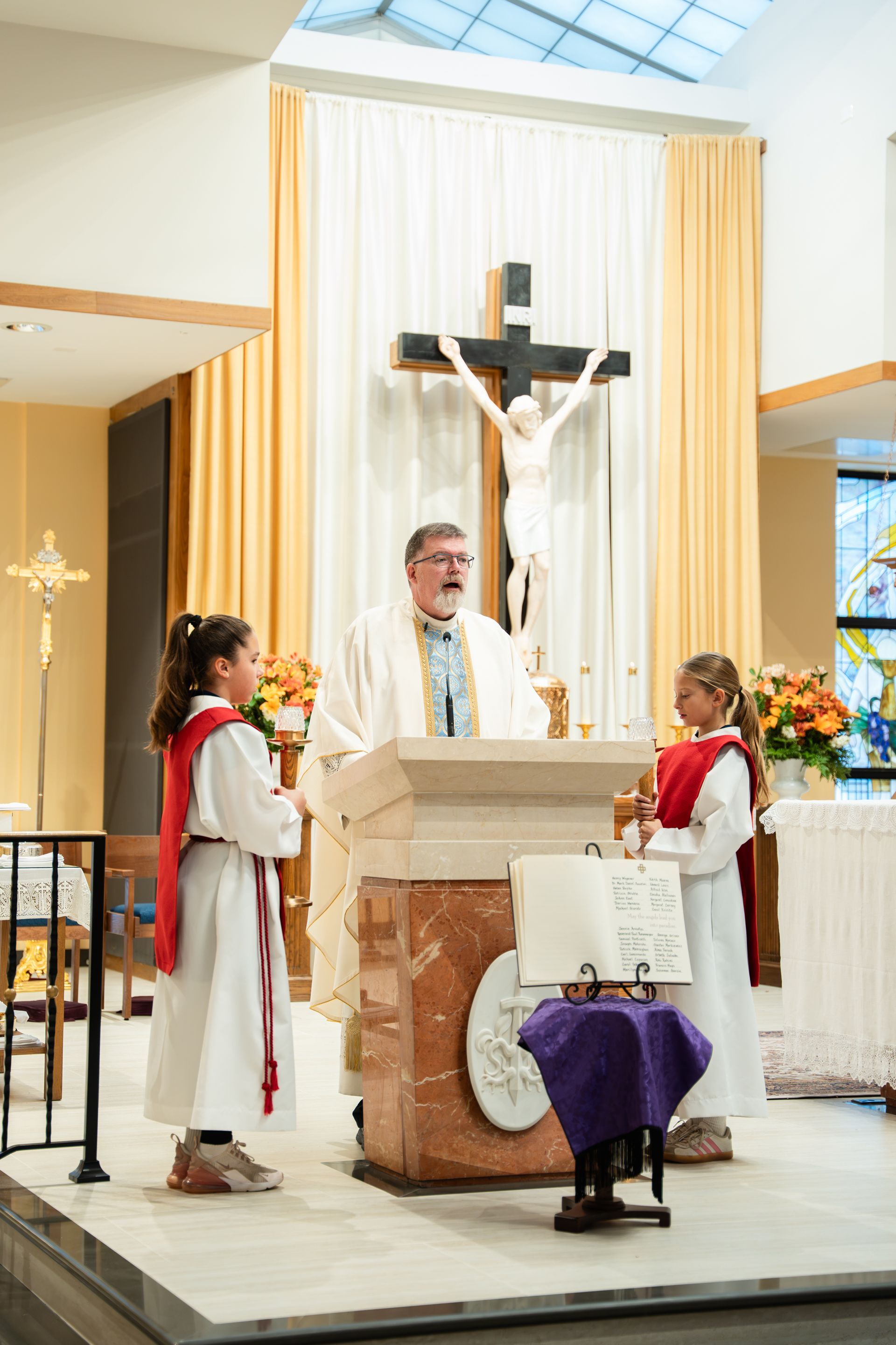 Clergy and altar servers stand at a church altar beneath a crucifix during Mass
