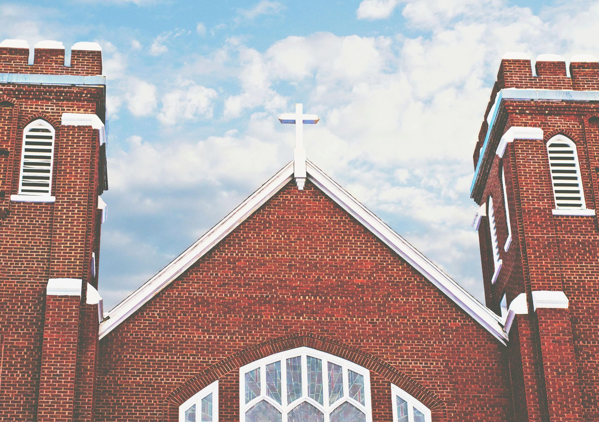 Red brick church facade with twin towers and a white cross on the roof