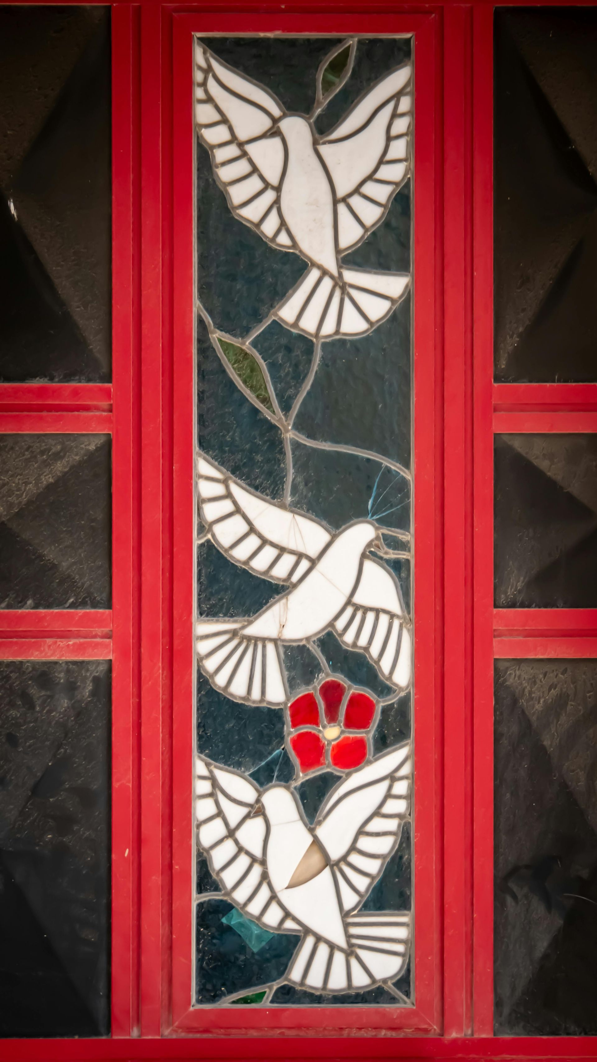Stained glass panel with white doves and a red paw print, framed in red and black