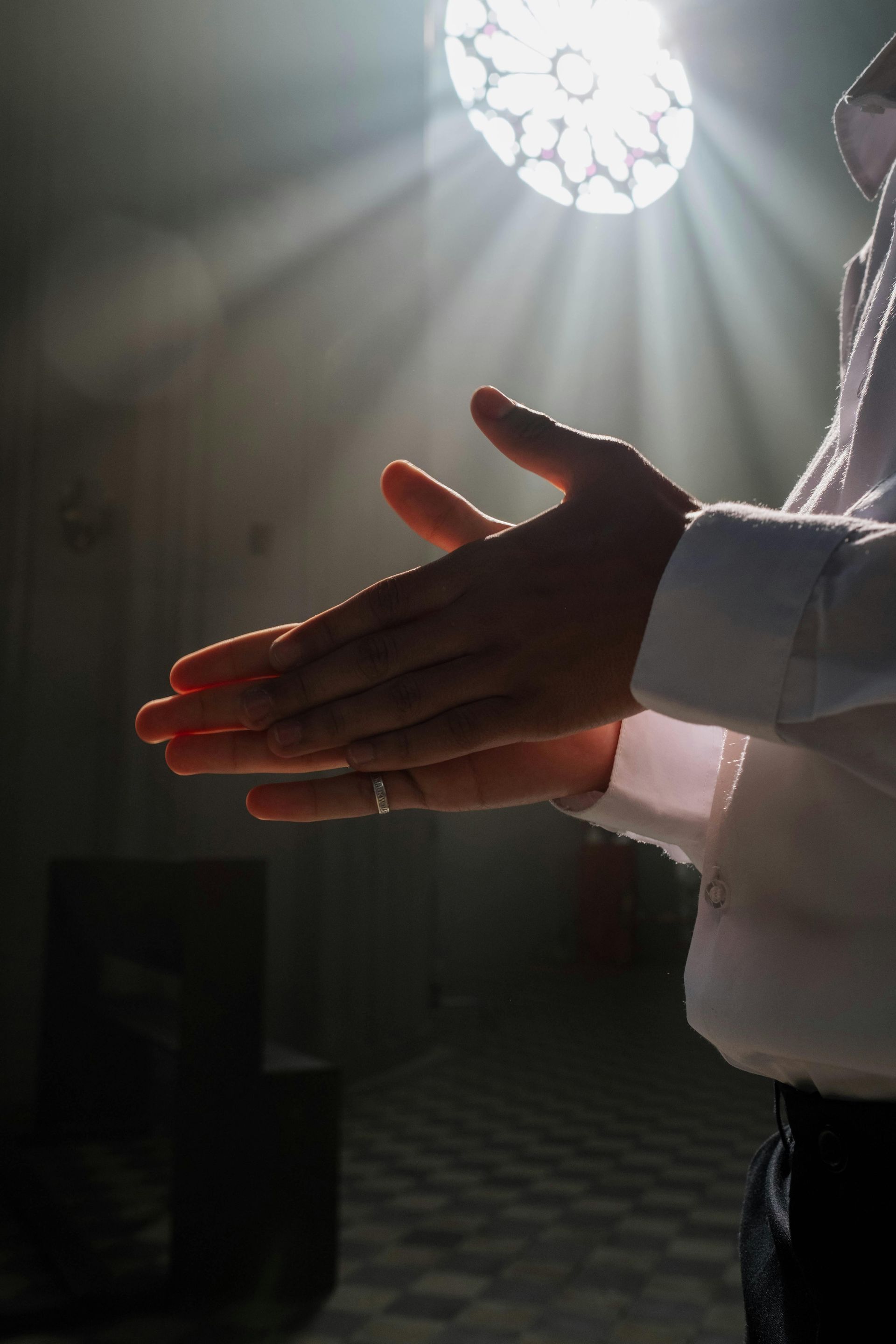 Hands clasped in prayer beneath bright sunlight streaming through a window