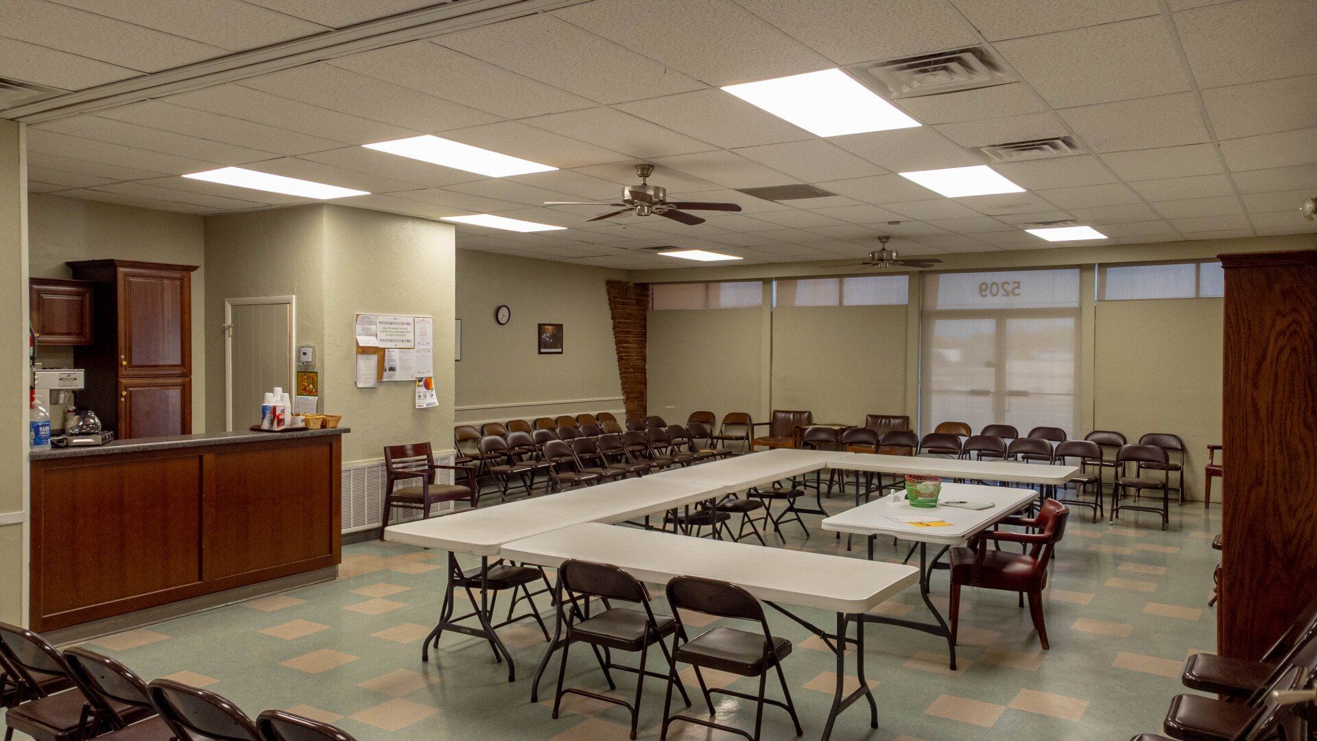 Meeting room with tables arranged in a U-shape, many chairs, and cabinets.