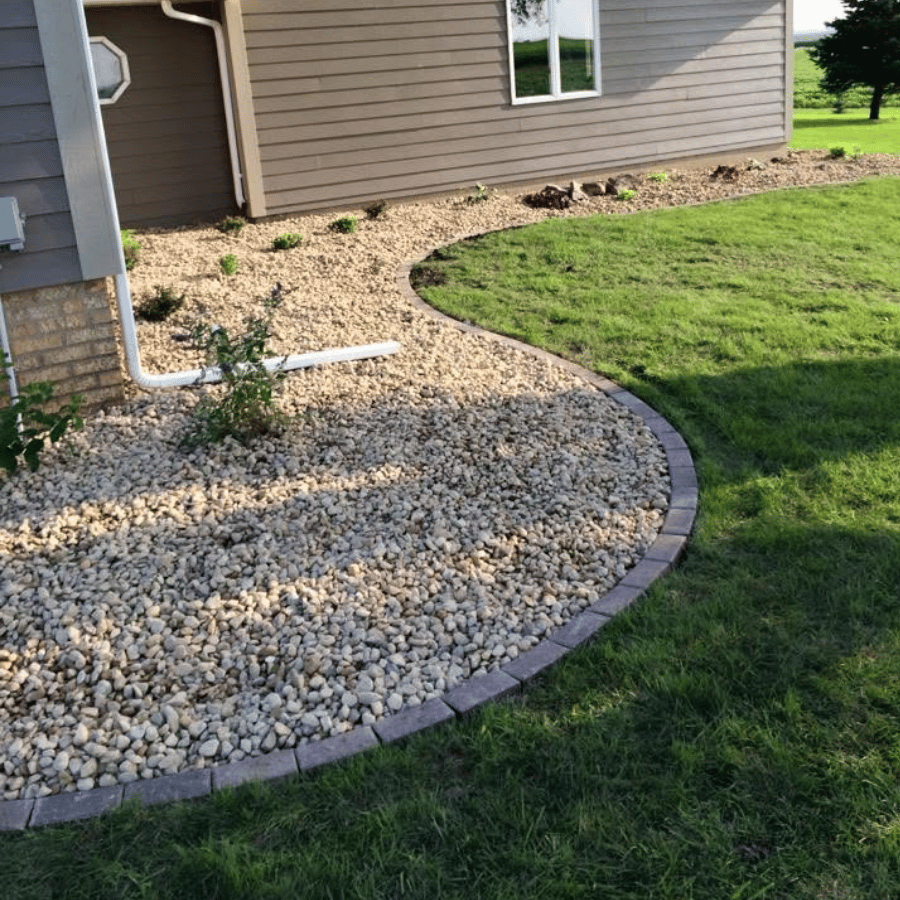 House exterior with brown siding, bordered by a curved stone path and lush green grass, under a clear blue sky.