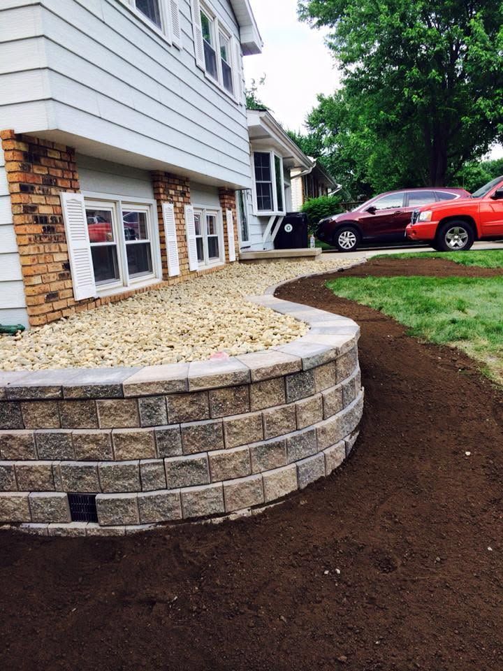 Front of house with stone retaining wall, mulch path, and parked cars in driveway