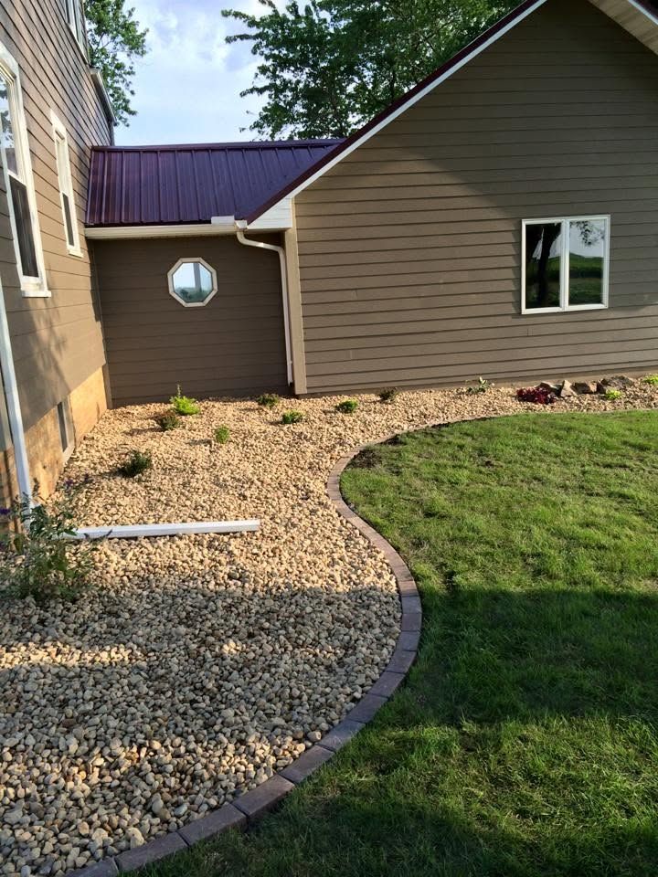 Backyard side yard with beige house, gravel path, mulched bed, and green lawn