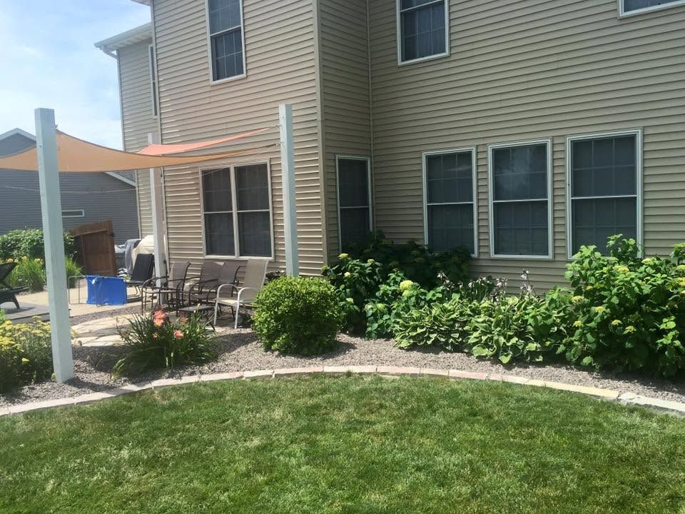 Backyard patio beside beige house with chairs, potted plants, and landscaped shrubs