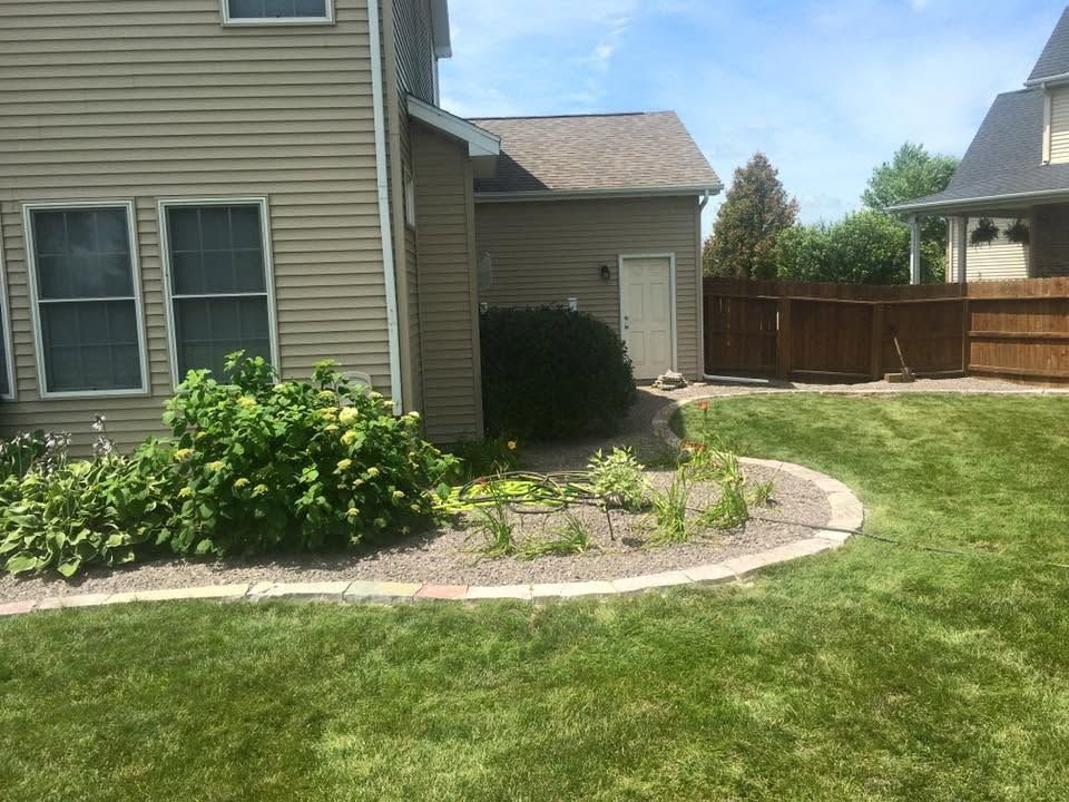 Suburban house exterior with landscaped front yard, curved stone border, and driveway by a wooden fence