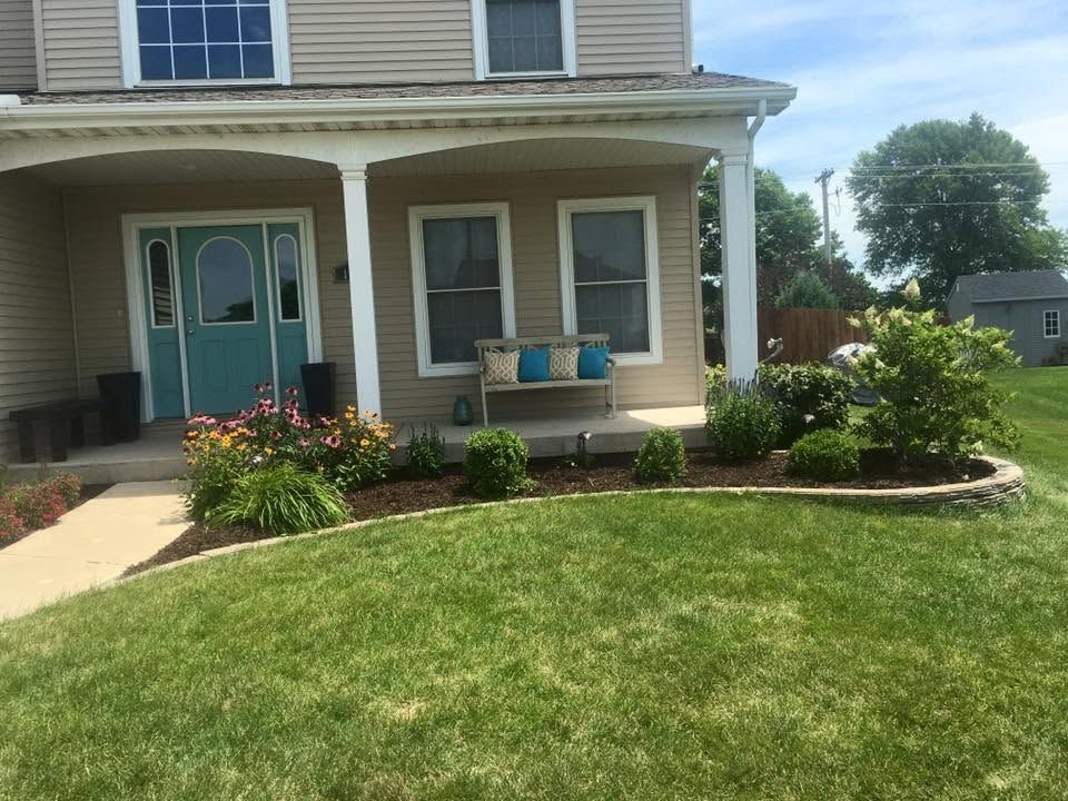 Front of a beige house with a blue door, flower beds, and a green lawn