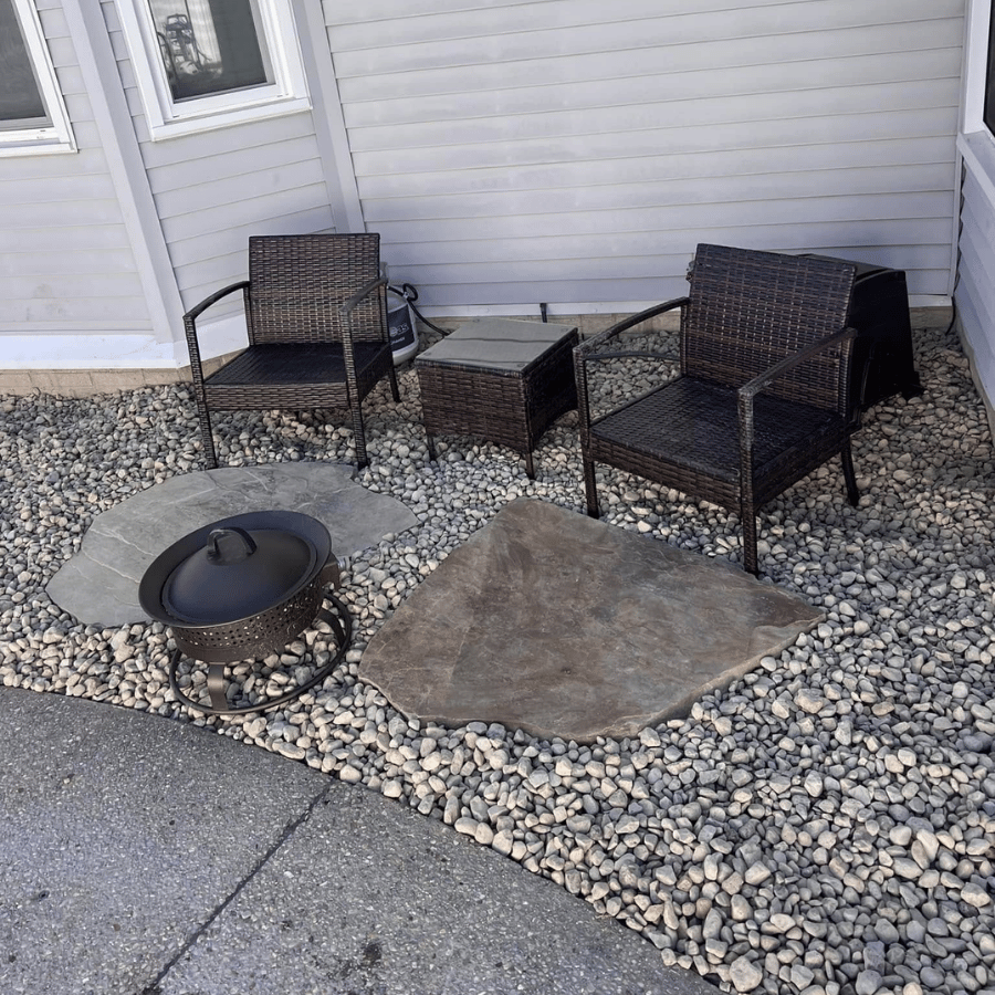 Patio seating area with two wicker chairs, small table, fire pit, and stone pavers beside a house