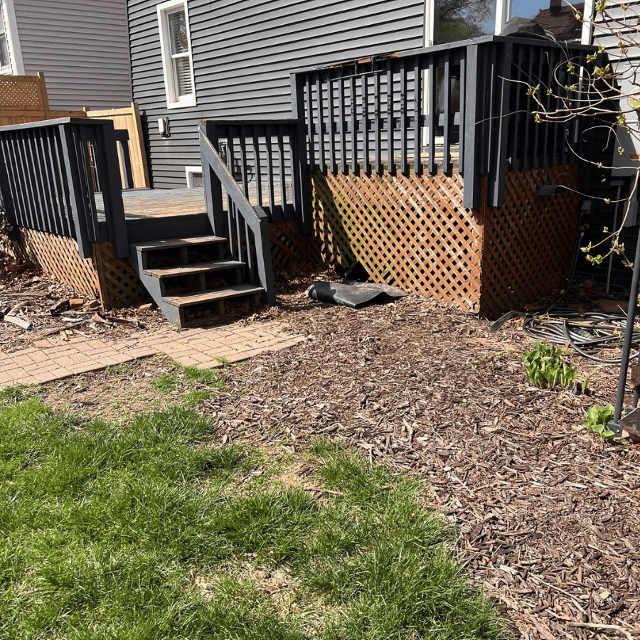 Backyard deck stairs with black railings, lattice skirting, and a mulched garden bed beside a house