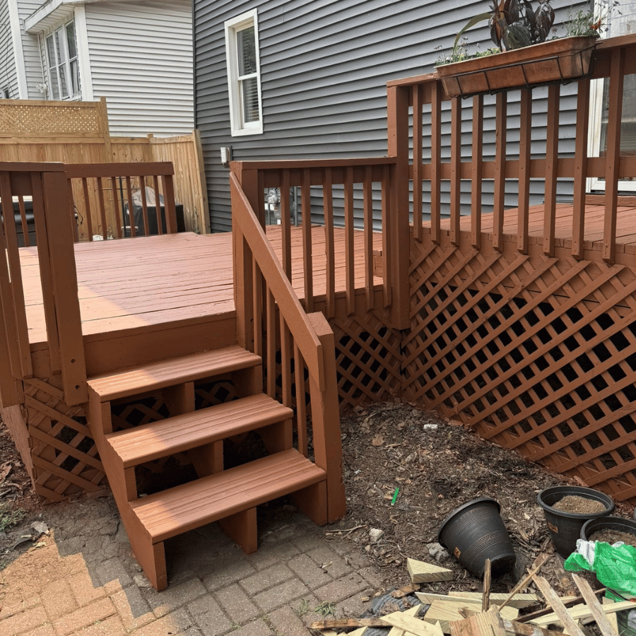 Backyard wooden deck with stairs, railings, lattice panels, and patio bricks beside a house