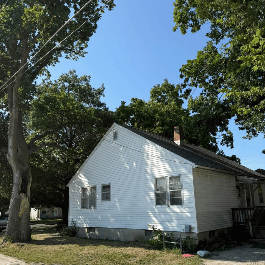 White house with a gabled roof under large trees on a sunny day