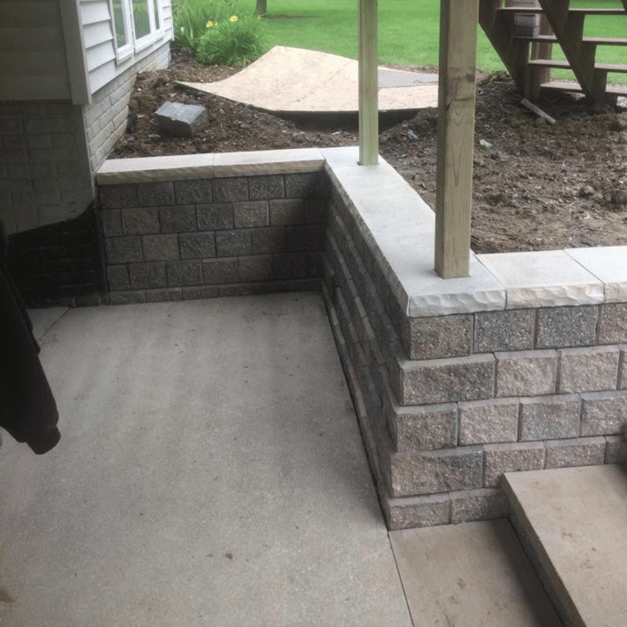 Newly built stone retaining wall and stairs beside a house, with fresh soil and grass in the background.