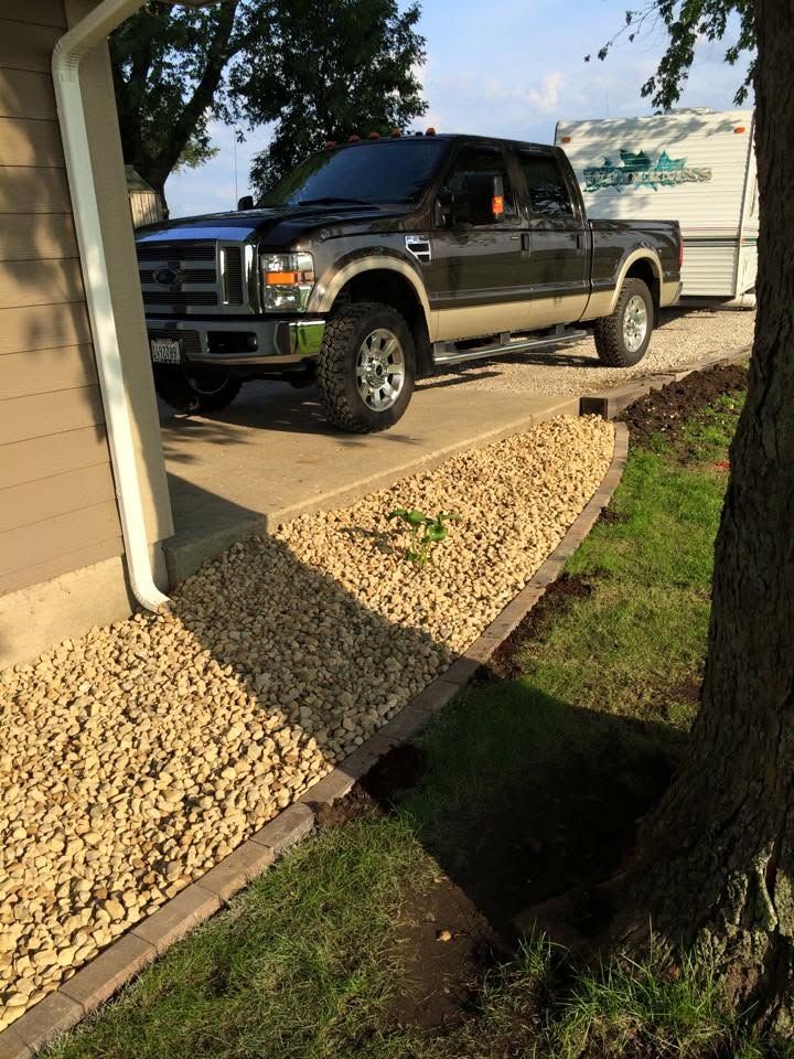 Black pickup truck parked in a driveway beside a house and gravel landscaping.