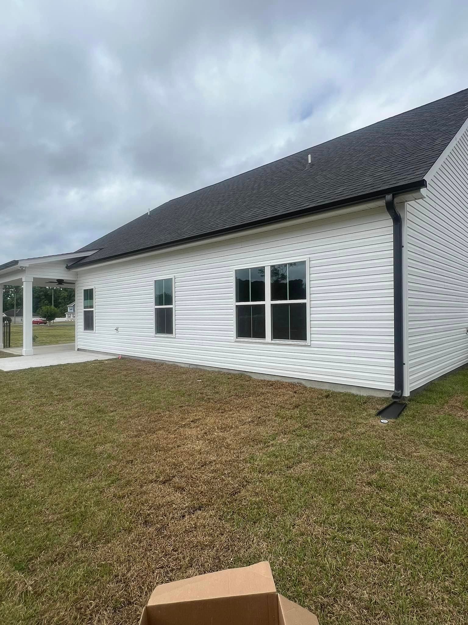 A white house with a black roof is sitting on top of a lush green field and newly installed gutter in Johnsonville