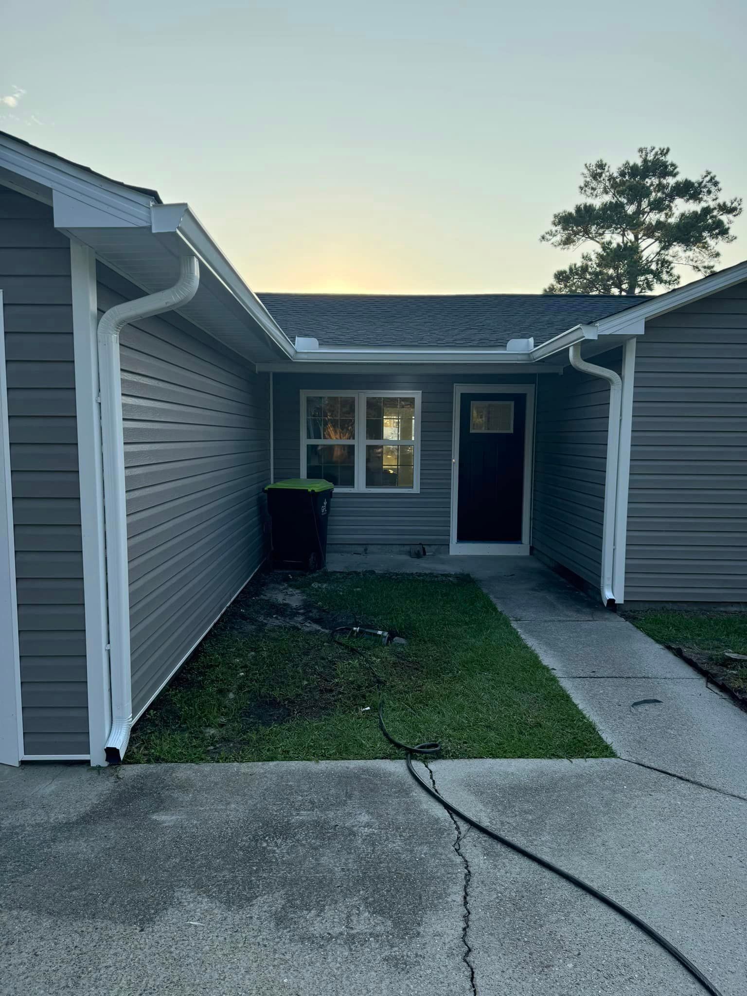 A small house with a porch, a lot of grass in front of it and newly repaired gutter in Galivants Ferry