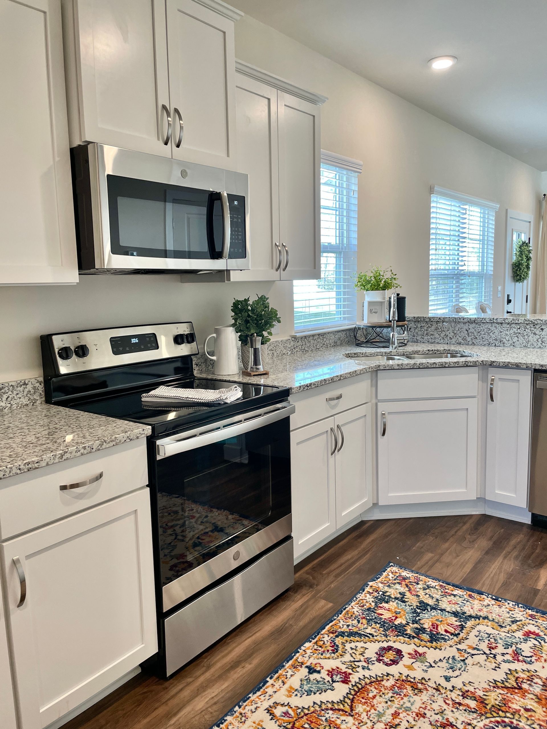 photo of kitchen at The Towns at Swift Creek showing white shaker cabinets, granite counters, wood plank flooring, and stainless steel appliances.