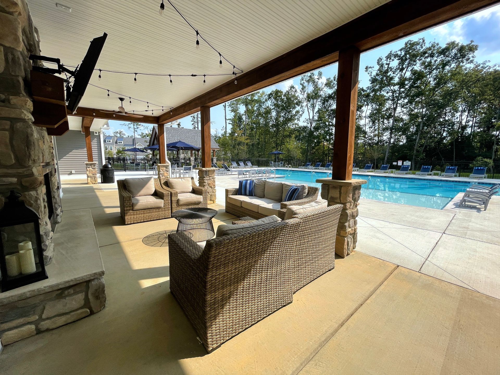 A patio with wicker furniture and a fireplace next to a pool.