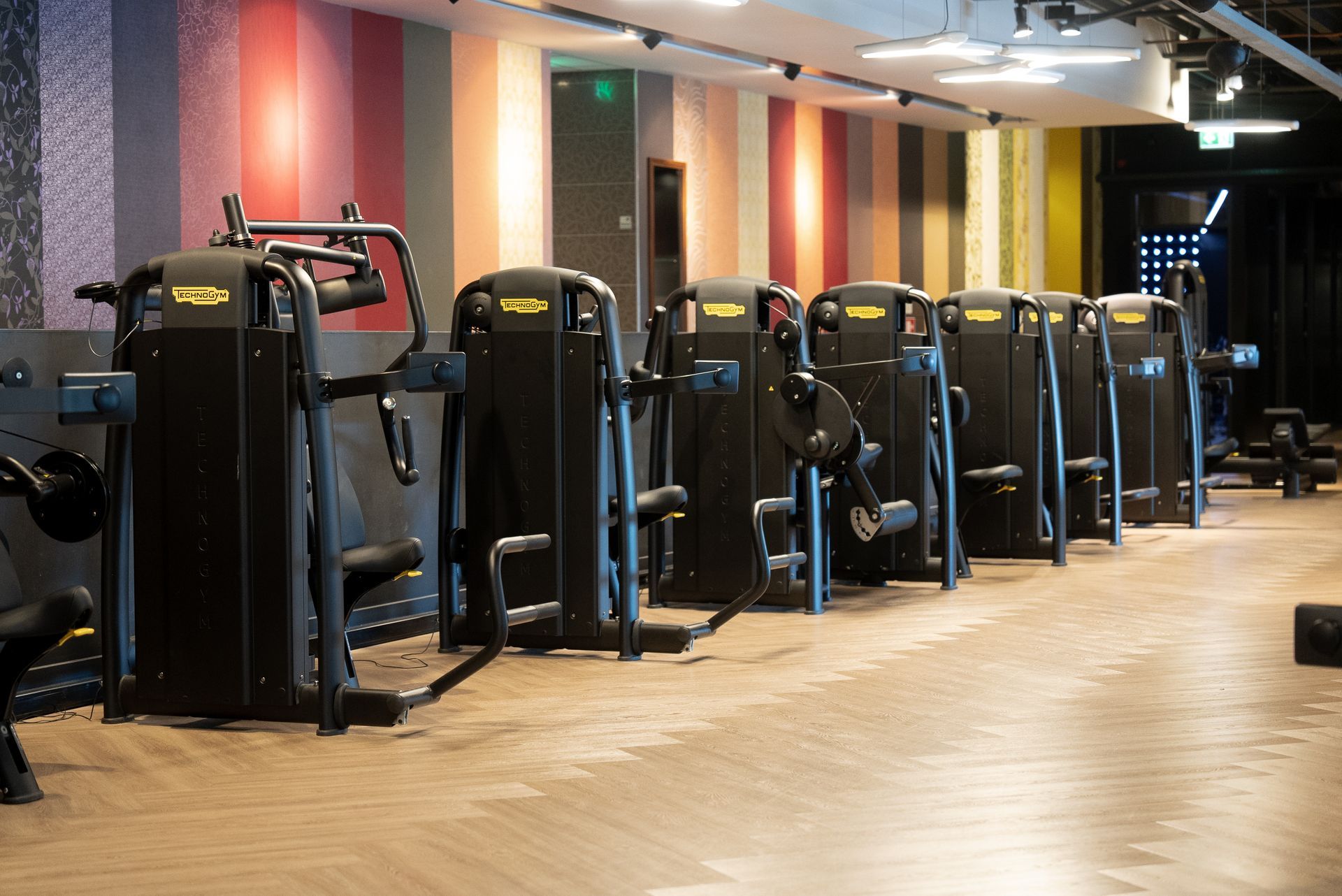 In een sportschool staat een rij fitnessapparaten opgesteld.