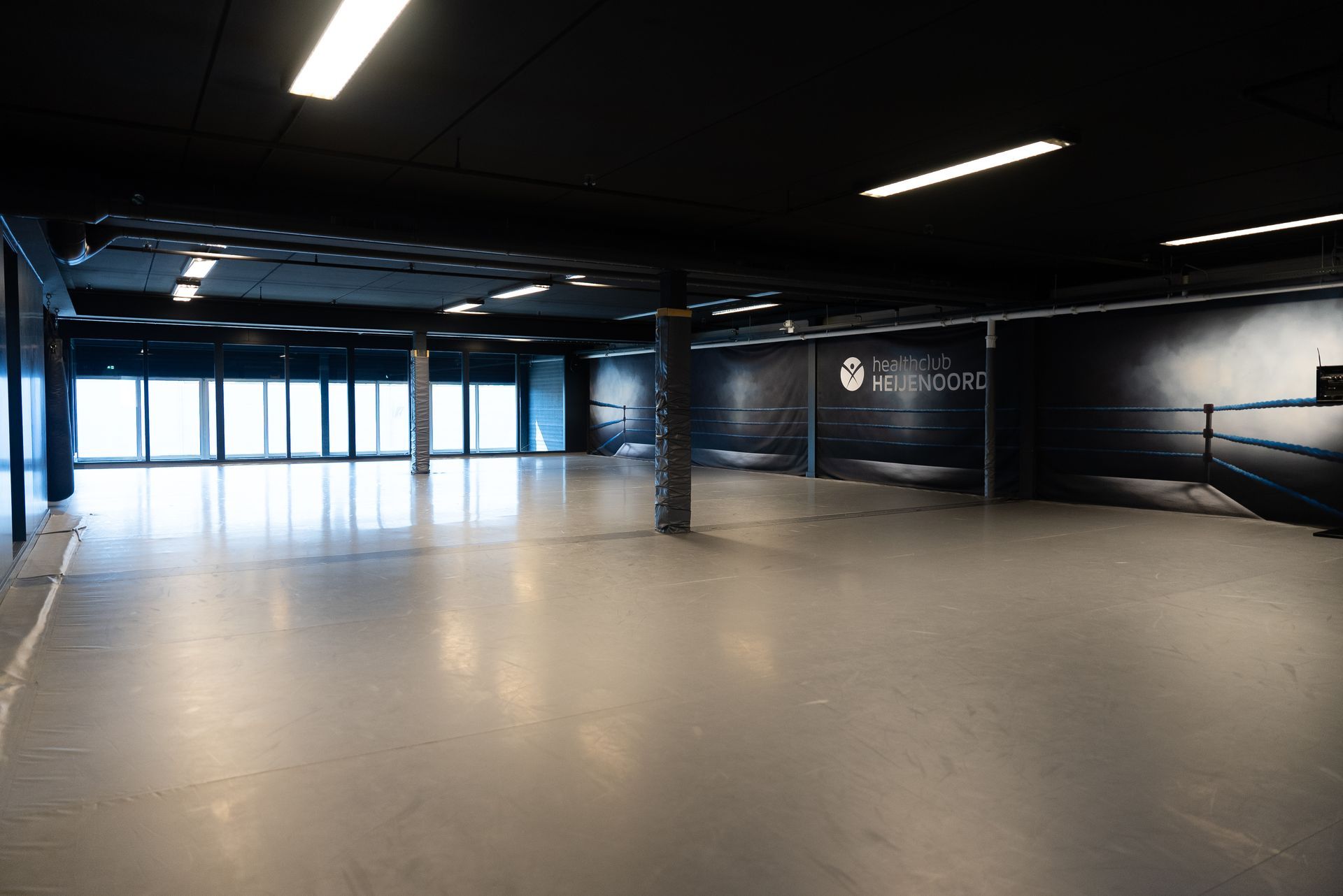Een grote lege kamer met veel ramen en een boksring.