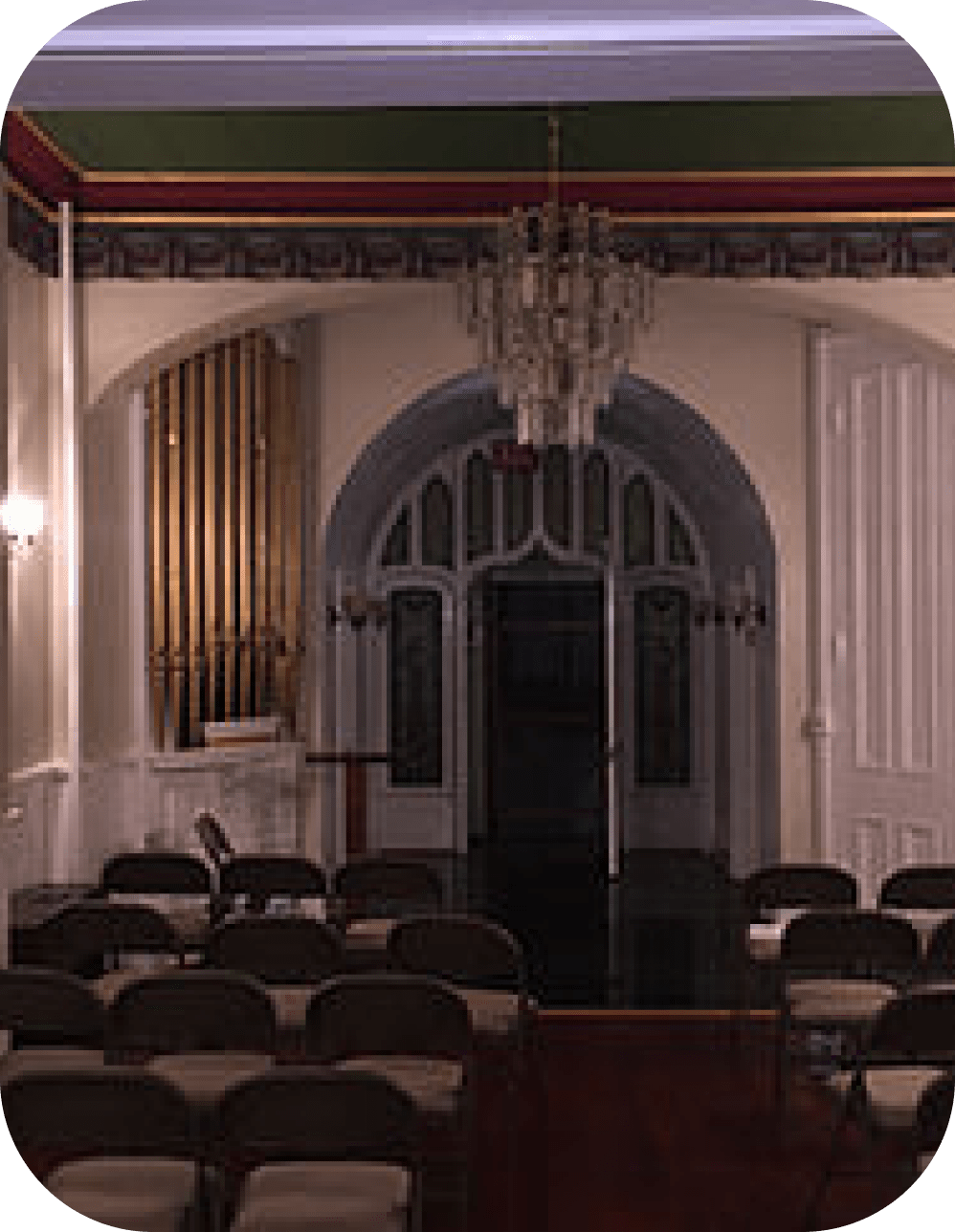 Empty ornate hall with chandeliers, arched doorway, and rows of chairs in the foreground