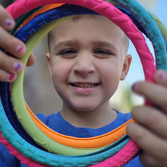 Child smiling through colorful stacked rings outdoors