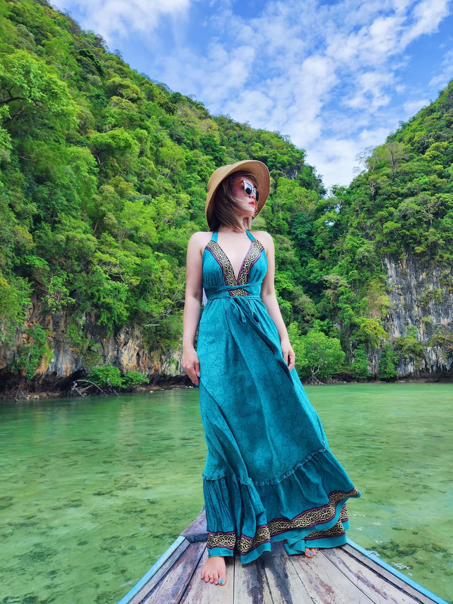 A woman in a blue dress is standing on a boat in the water.