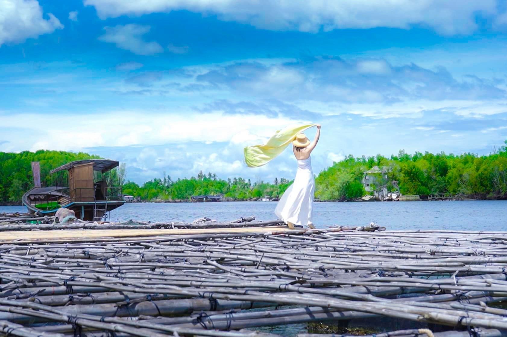 A woman in a white dress is standing on a wooden platform overlooking a lake.