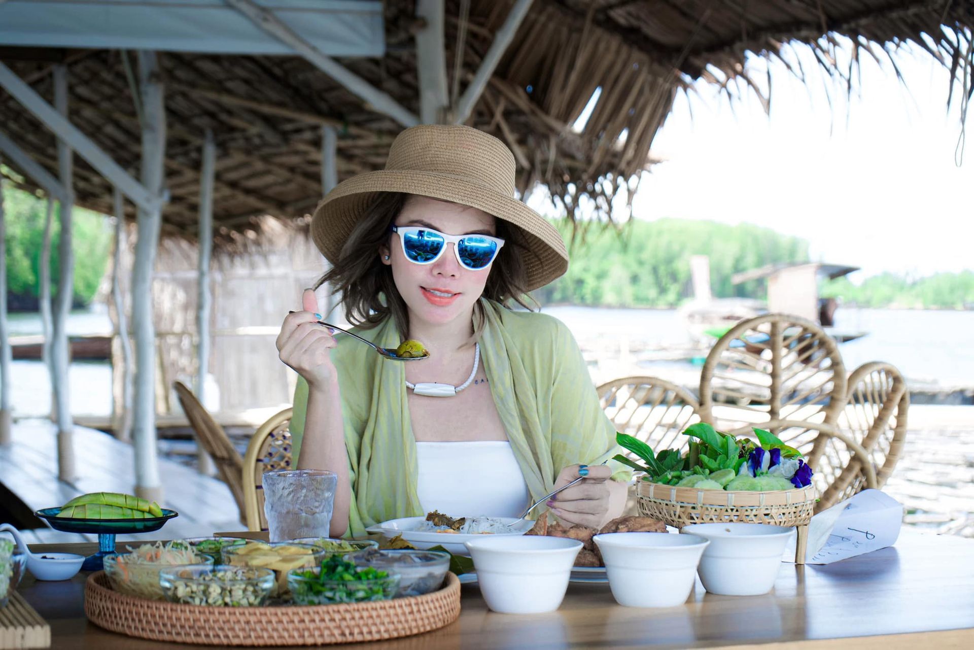 A woman wearing a hat and sunglasses is sitting at a table eating food.