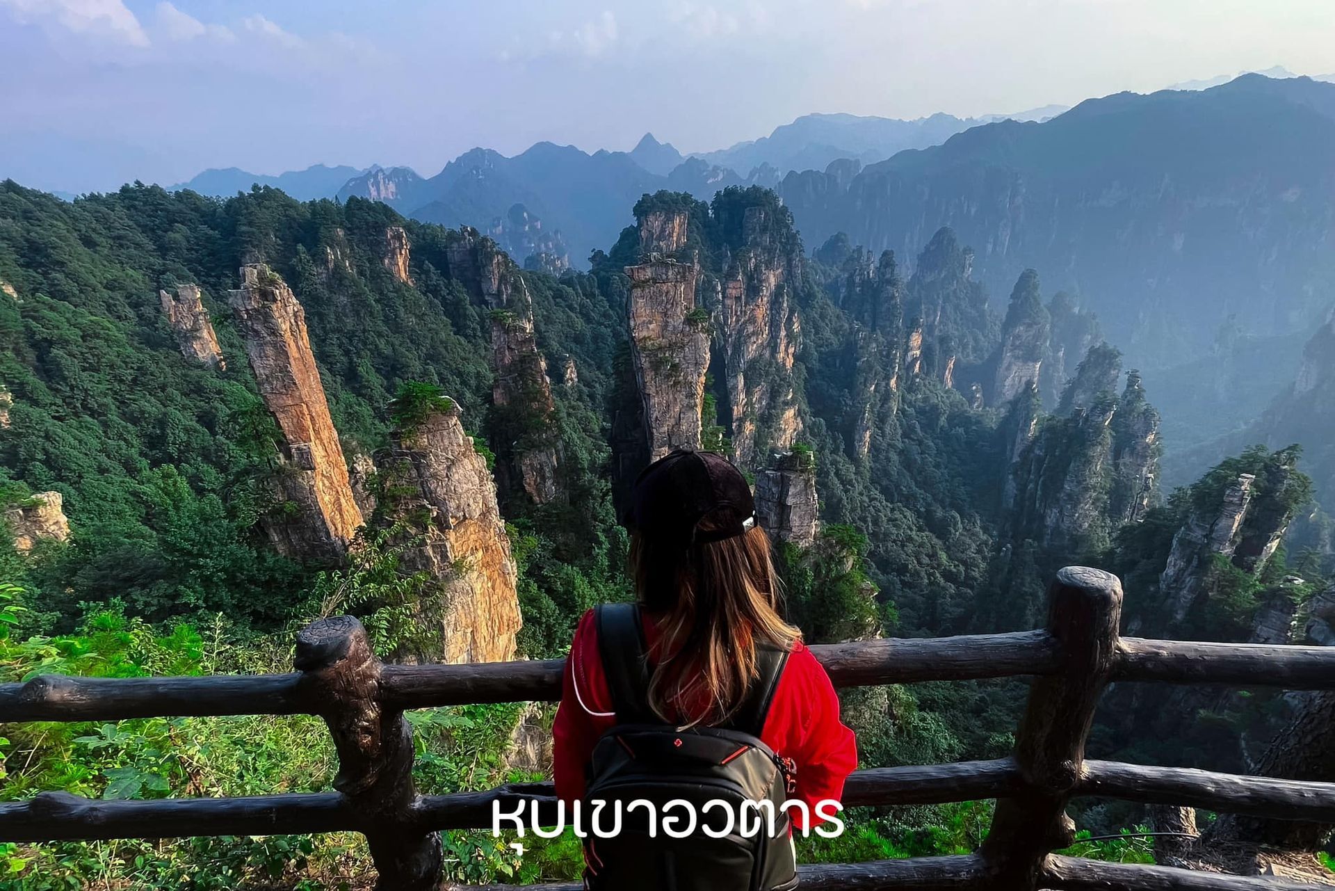 A woman is standing on a balcony overlooking a mountain range.